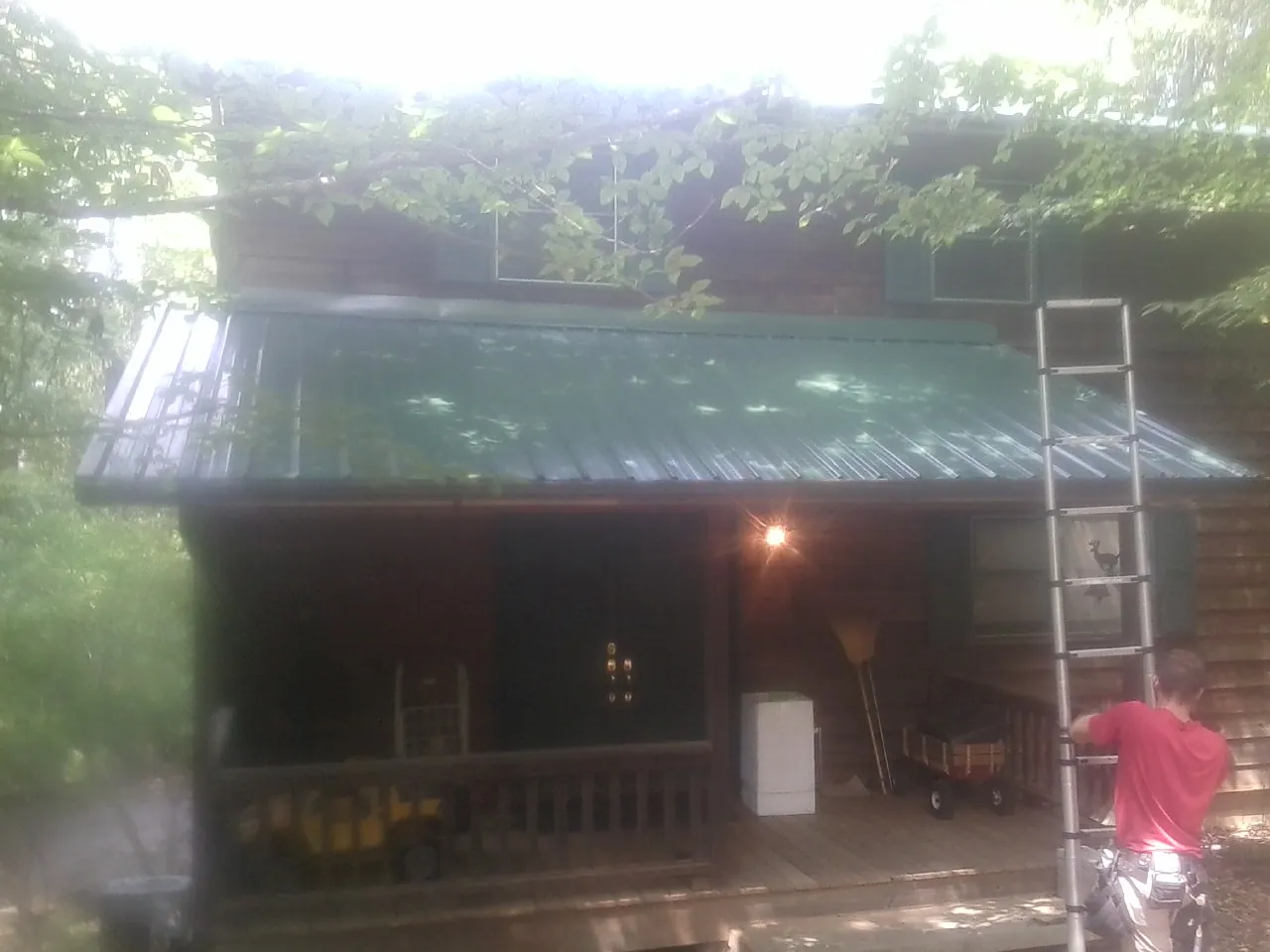Worker on a ladder at the green porch roof of a wooded cabin in Edgewater